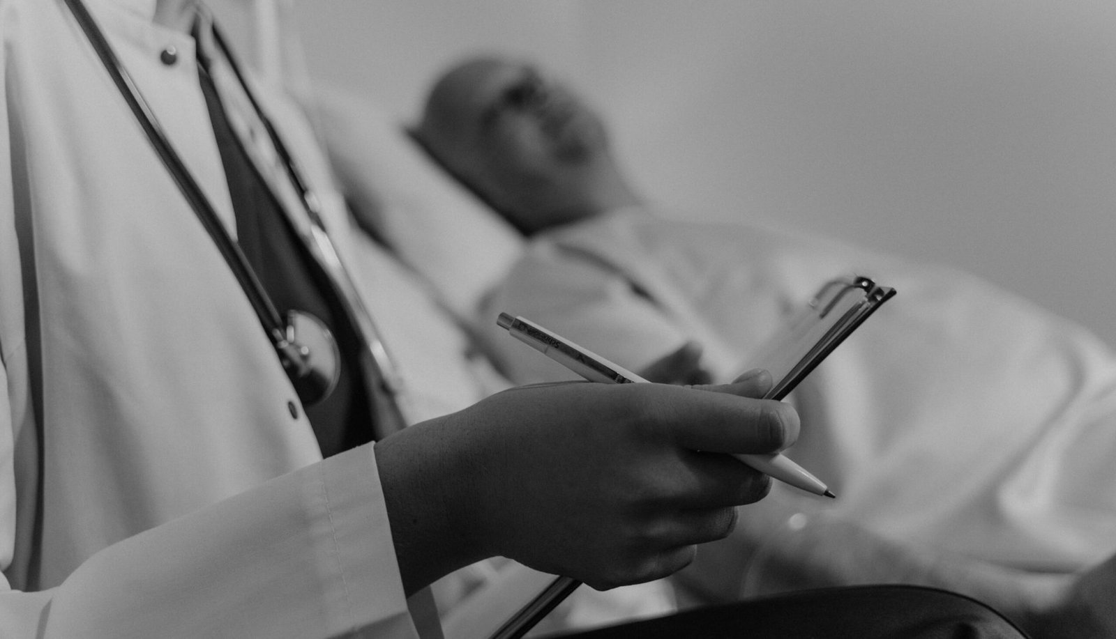 A doctor takes notes while consulting a patient in a hospital setting.
