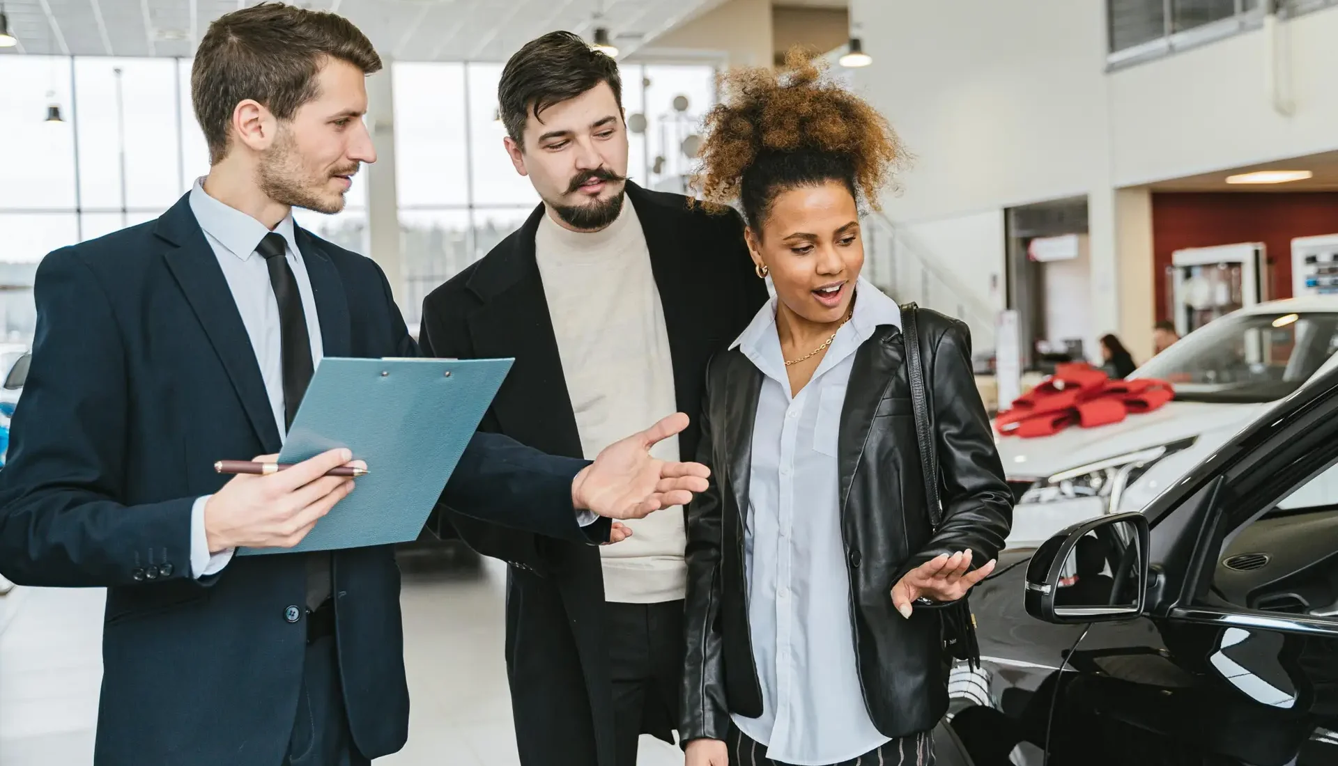 A diverse group of adults discussing vehicles at a bright modern car dealership.
